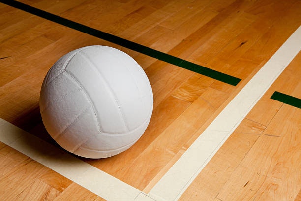 A volleyball on a wooden court with line markings.