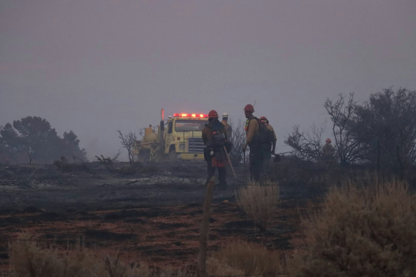 Firefighters on a smoky landscape with a fire truck in the background.