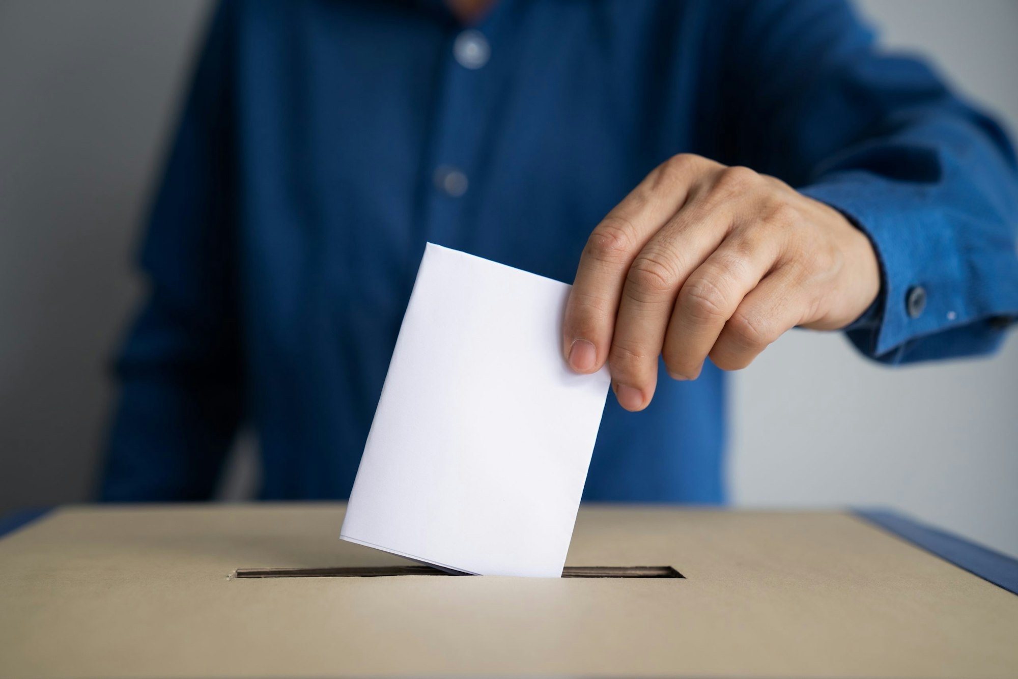 A person is casting a vote by placing a ballot into a ballot box.