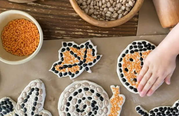 Child's hand decorating dough shapes with various beans and lentils.