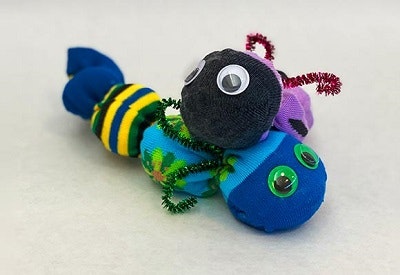 A colorful, homemade sock creature with googly eyes and pipe cleaner antennae.