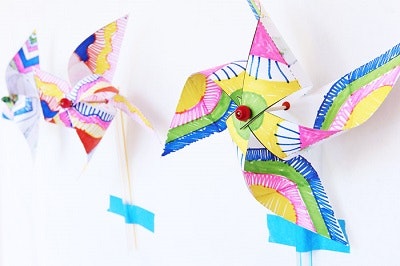 Colorful paper pinwheels attached to sticks, secured with blue tape on a wall.