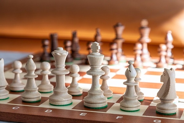Chessboard with wooden pieces arranged, white pieces in focus, warm lighting.