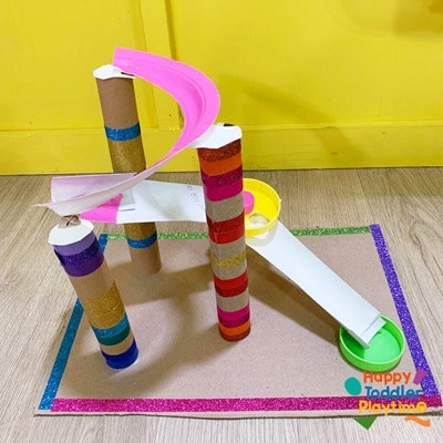 A colorful homemade marble run made of cardboard tubes and ramps, featuring glitter and playful design elements.