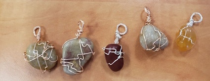 Five stones wrapped in different styles of wire on a wooden surface.