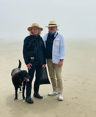 Two people wearing hats and a dog on a foggy beach.