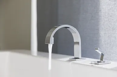 Modern kitchen faucet and sink handle on white countertop with gray backsplash.