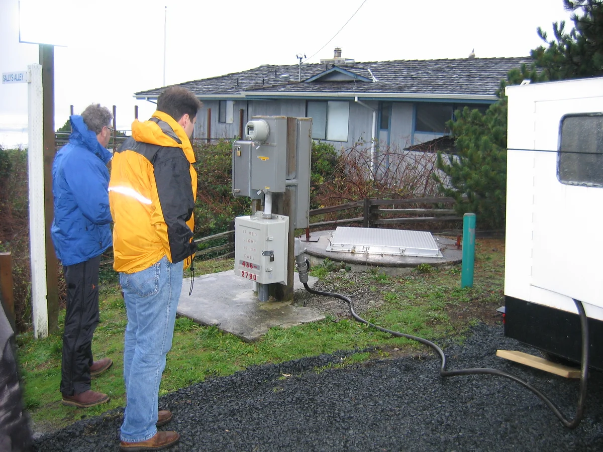 Two individuals observing an outdoor electrical installation near a house.