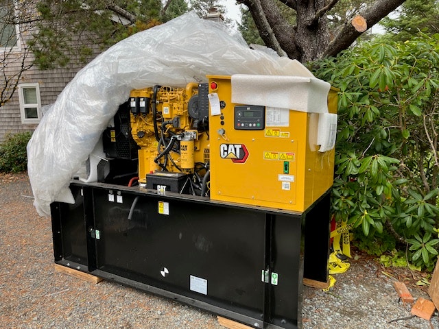 A CAT brand generator covered with plastic for protection, possibly newly installed outdoors.