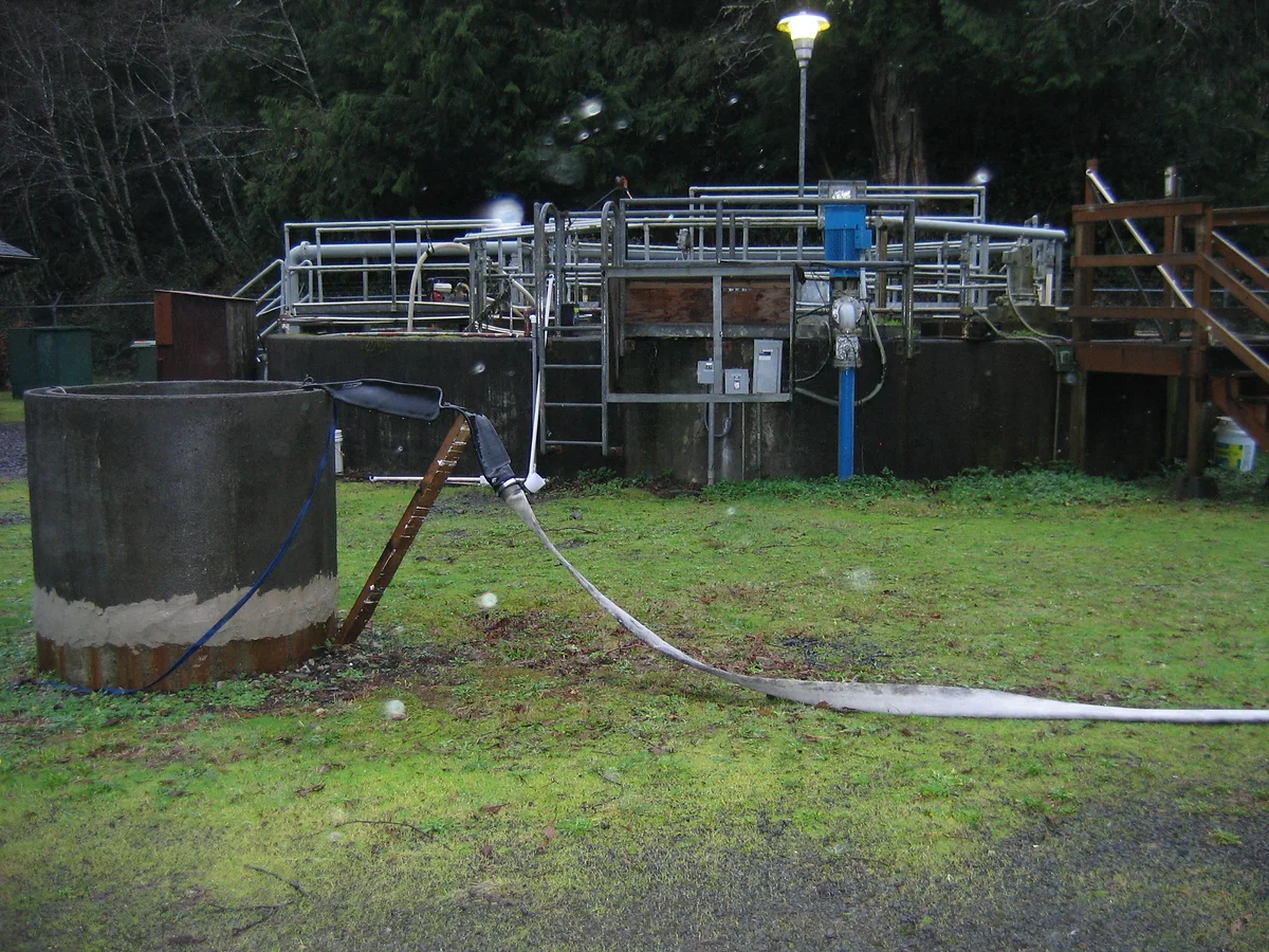 An outdoor wastewater treatment facility with tanks, hoses, and equipment.