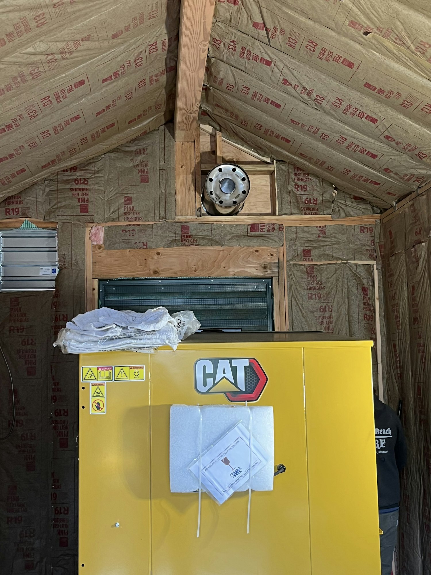 A yellow CAT generator, insulation, wooden beams, exhaust fan, face mask, and a partial view of a person.