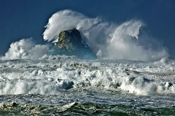 Massive waves crashing over a rock in the ocean.