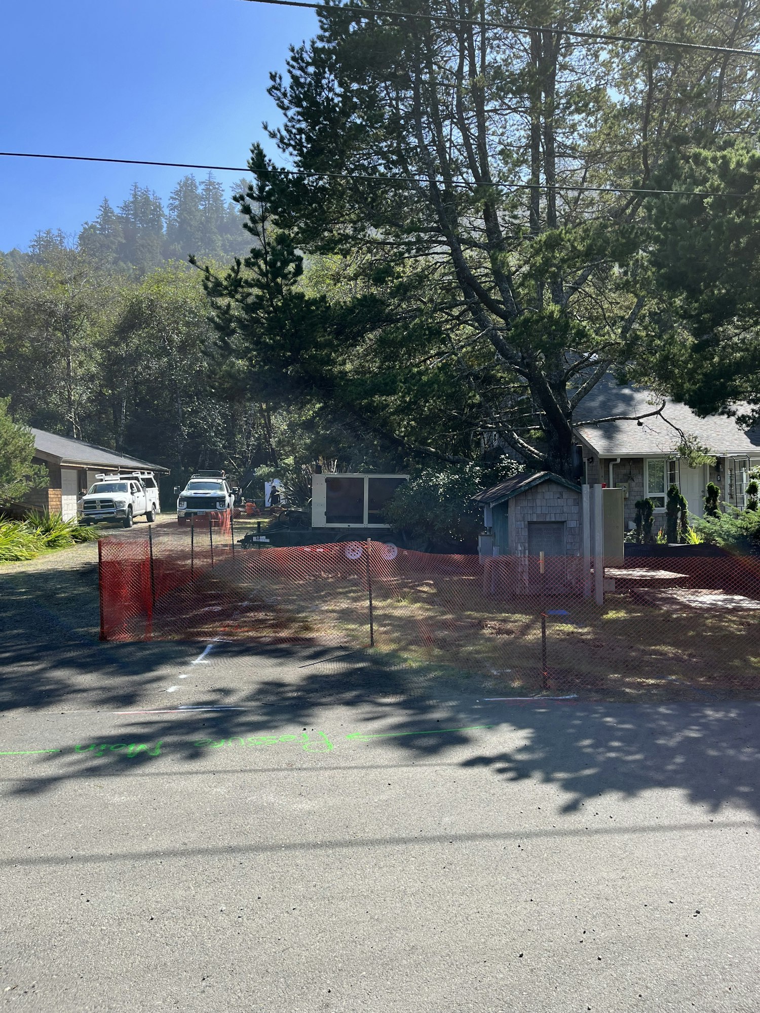 A sunny residential area with trees, houses, vehicles, and a red construction barrier.