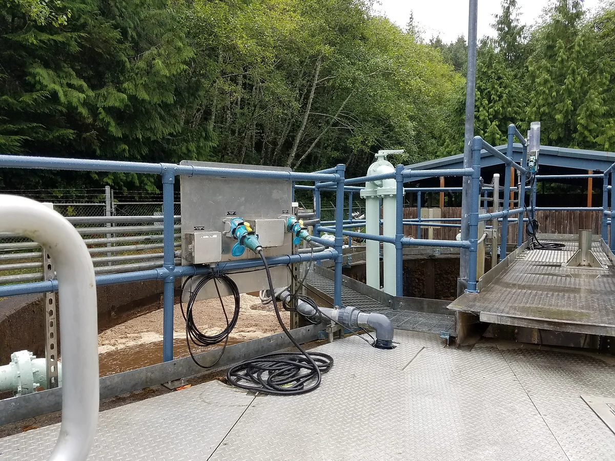 Industrial water treatment facility with metal walkways, pipes, and forest background.