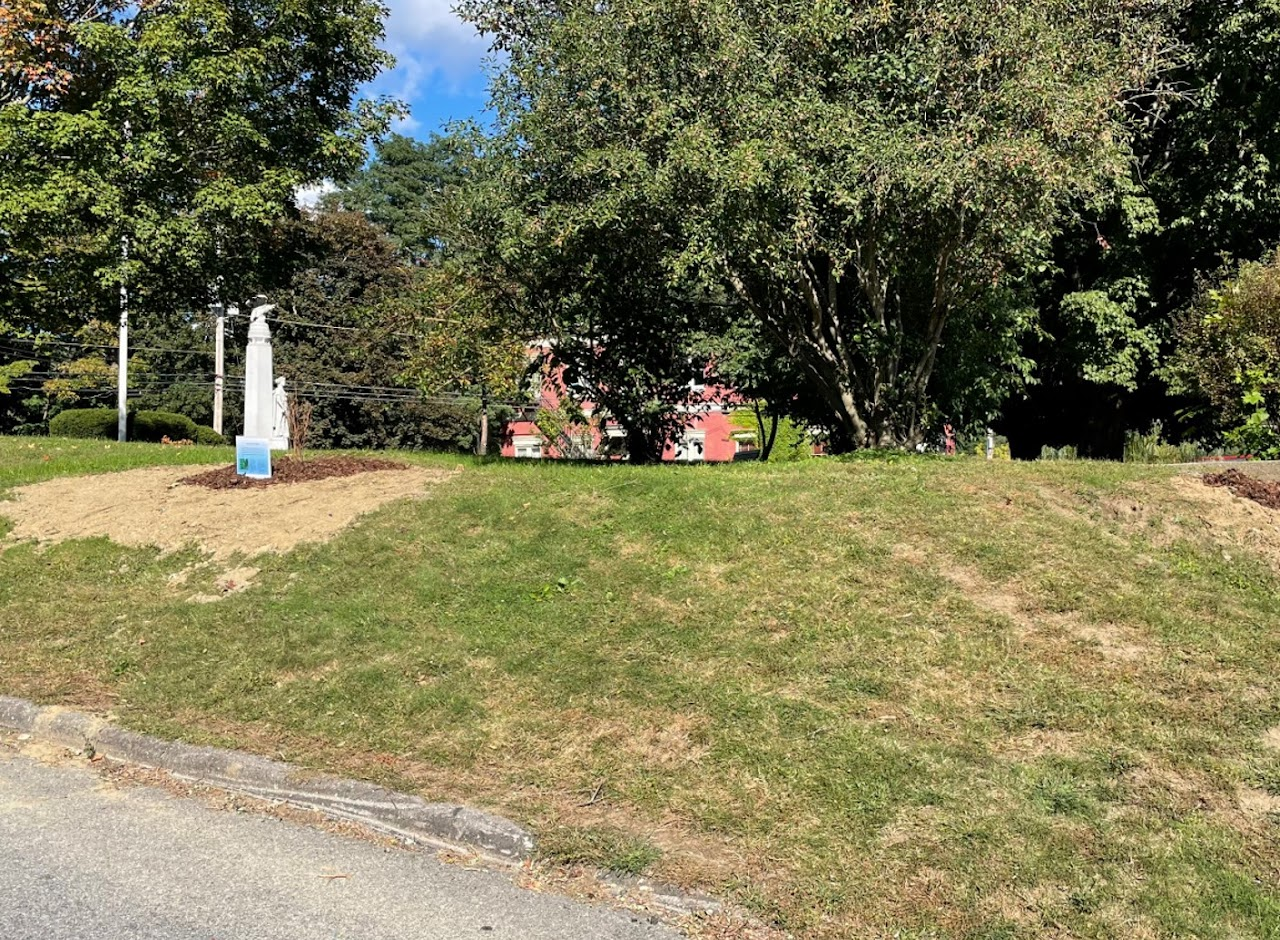 Grassy area, trees, lamp posts, red building in the background, and a blue sign.