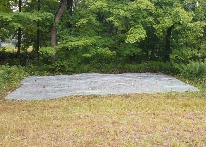 A large tarp on grass with trees in the background.