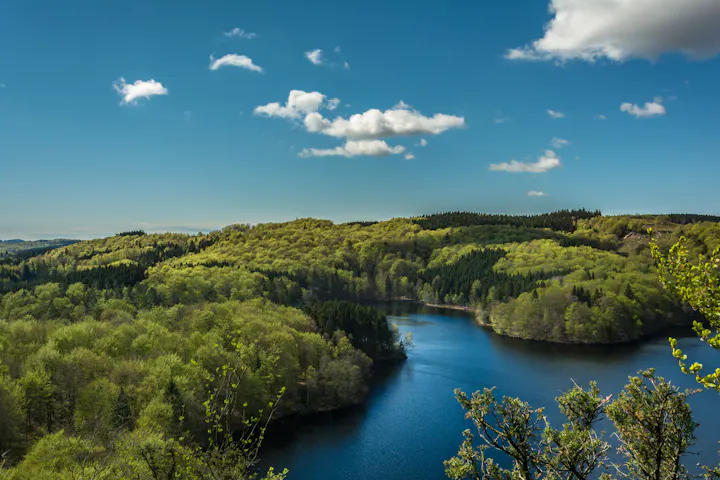 A scenic view of lush green hills surrounding a serene blue lake under a clear sky with a few clouds.