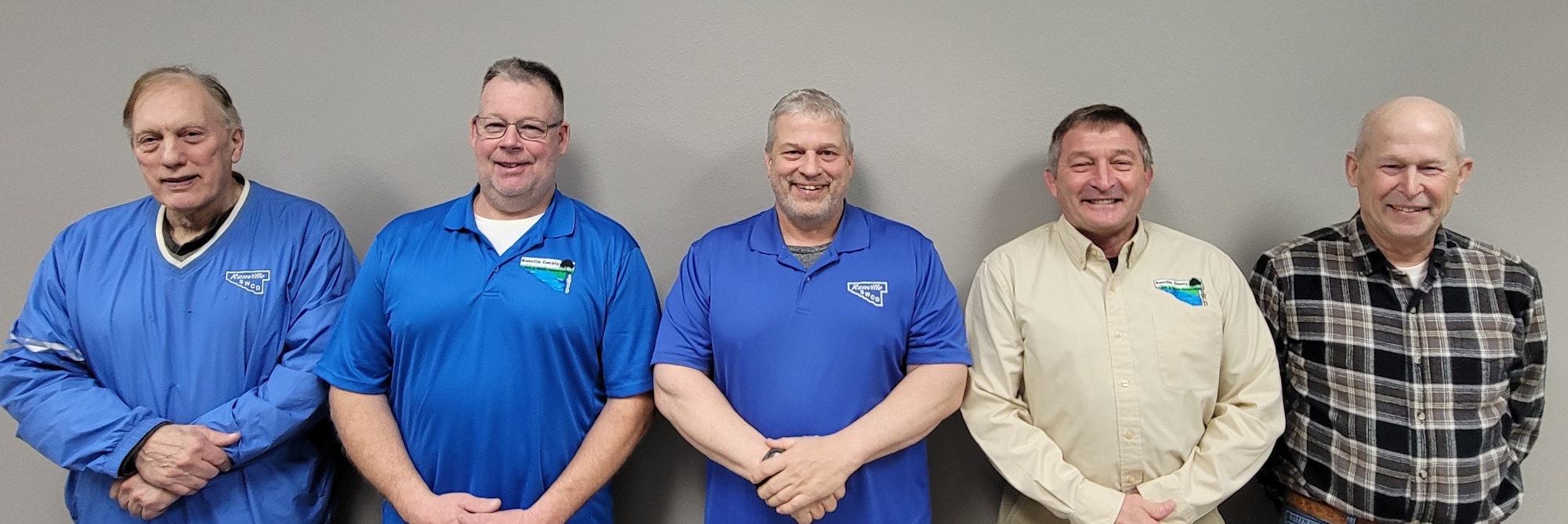 The Renville SWCD 2025 board members, smiling, standing against a gray wall, wearing blue and plaid shirts.