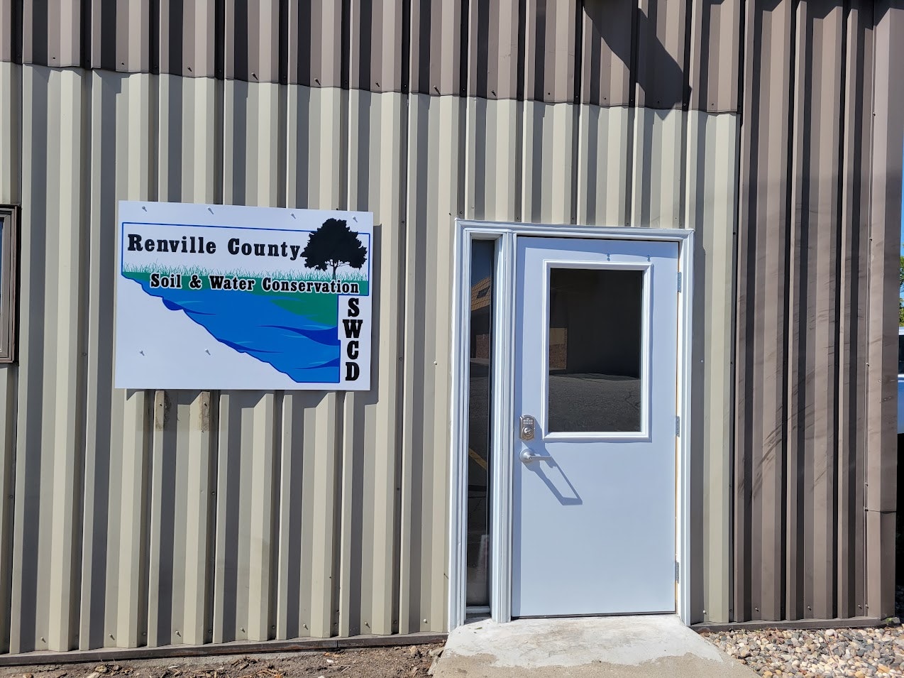 A sign reads "Renville County Soil & Water Conservation" next to a door on a corrugated metal building.