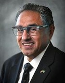 A person wearing glasses and a suit, smiling in a portrait photo with a gray background.