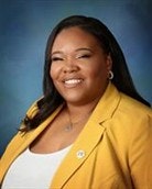 A person smiling, wearing a yellow blazer and white top, on a blue background.