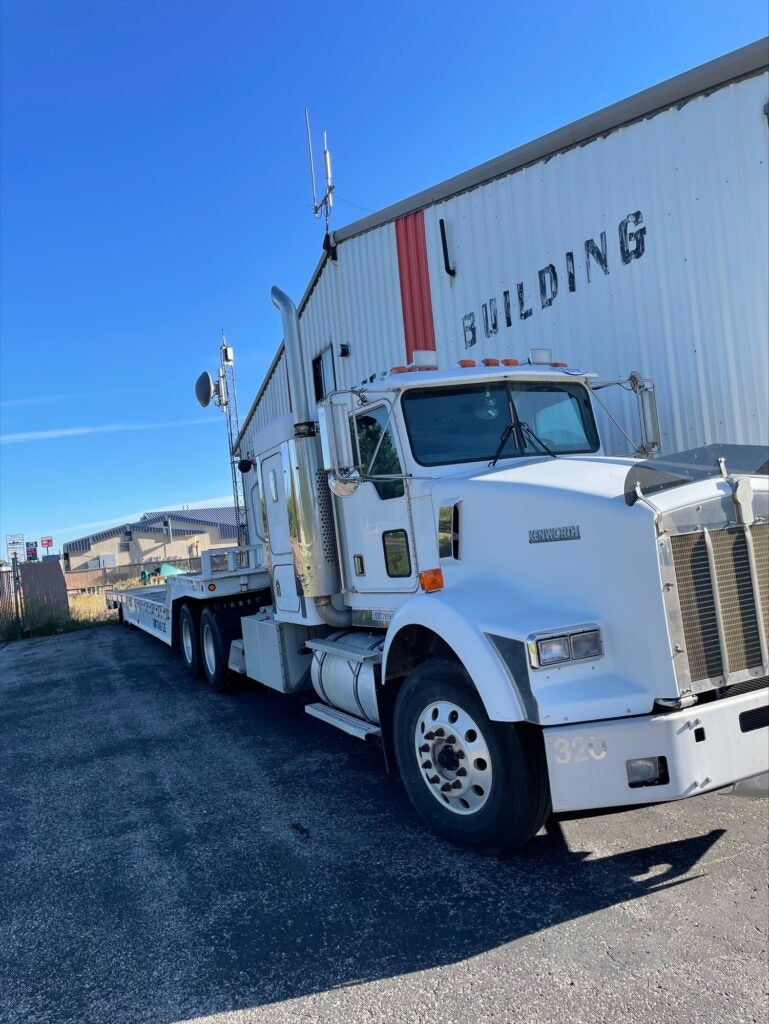 White semi-truck parked by a building with "L BUILDING" sign.