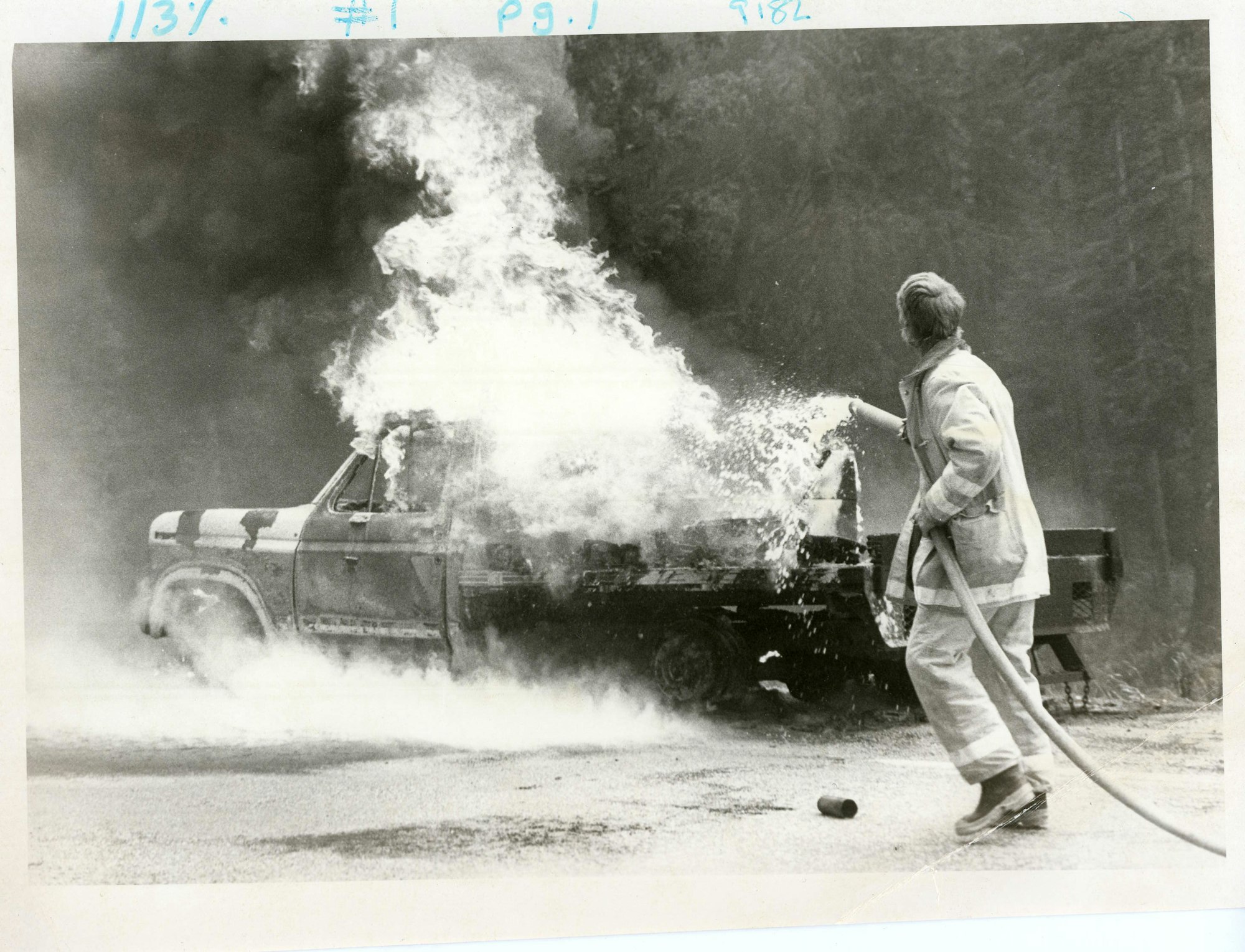 A firefighter is using a hose to extinguish a fire engulfing a vehicle.