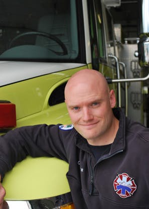 A bald man in a paramedic uniform in front of an ambulance.