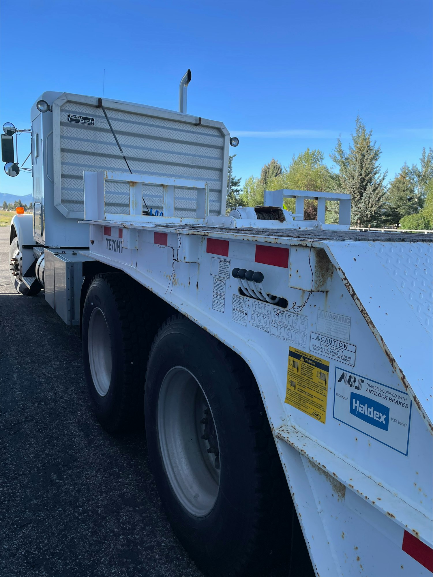 A close-up side view of a semi-truck with a white cab and a flatbed trailer under a clear sky.