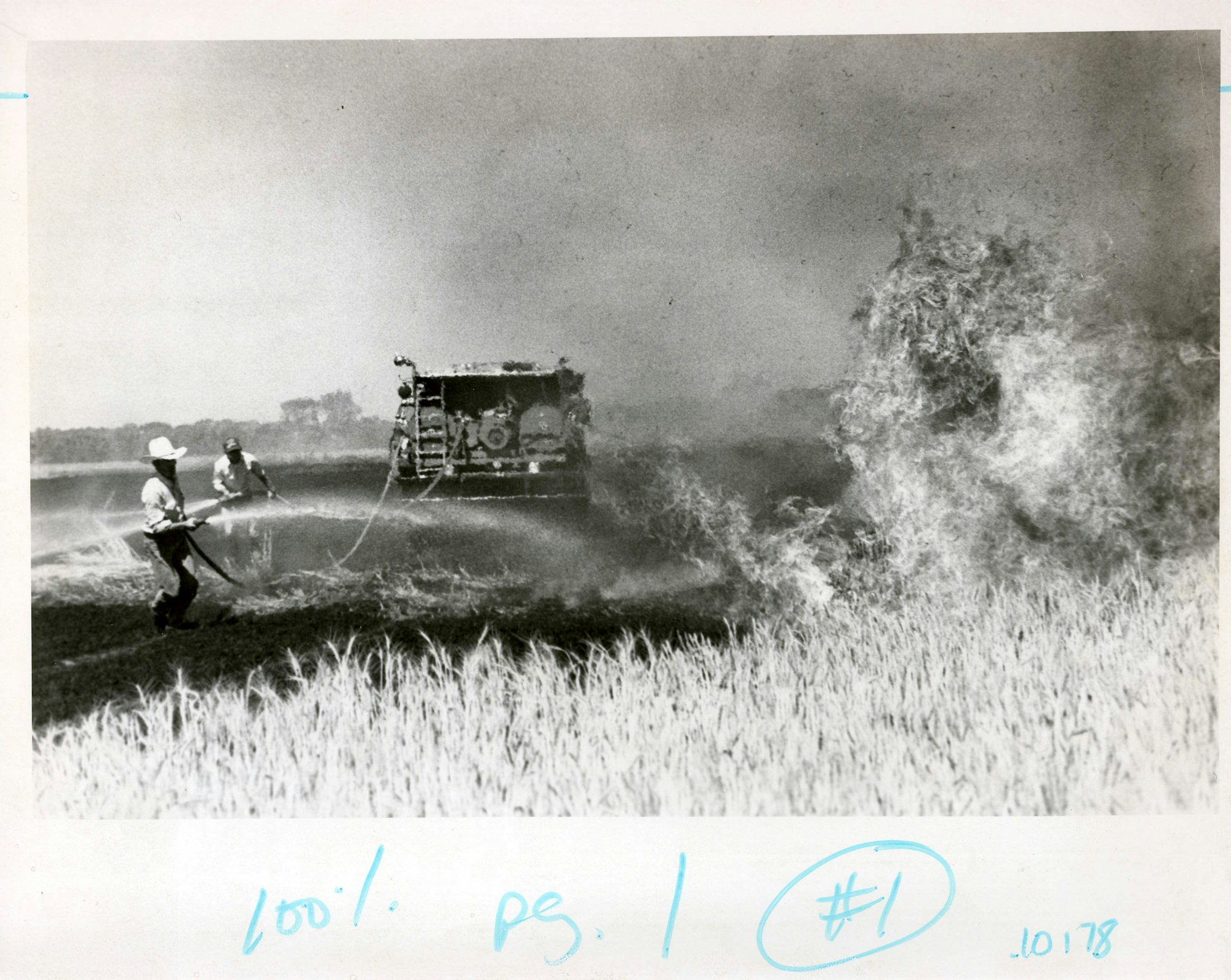 Firefighters extinguishing a blaze, smoke billowing, field in background, handwritten notes on photo.