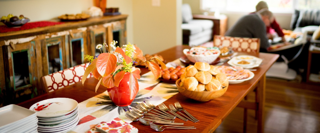 A dining table with plates, silverware, a flower centerpiece, food items, and a person in the background.