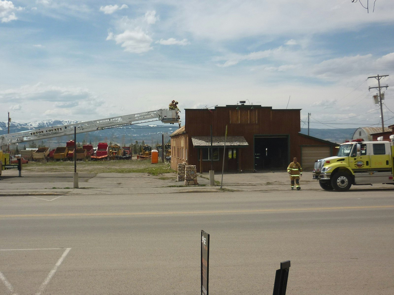 A fire truck with an extended ladder, firefighters, a building, and mountain scenery in the background.