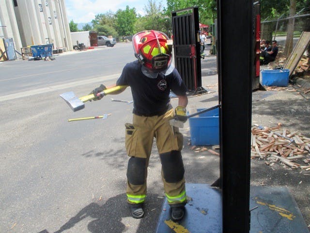 A person in firefighter gear holding a tool during training.