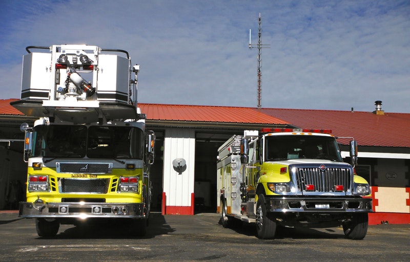 Two fire trucks in front of a fire station under a blue sky.