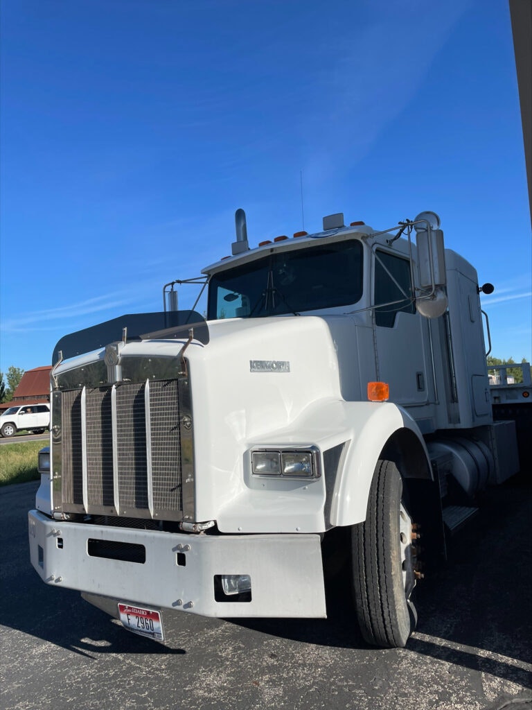 A white Kenworth semi-truck parked under clear blue skies.