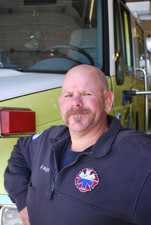 A firefighter in uniform standing in front of a fire truck.