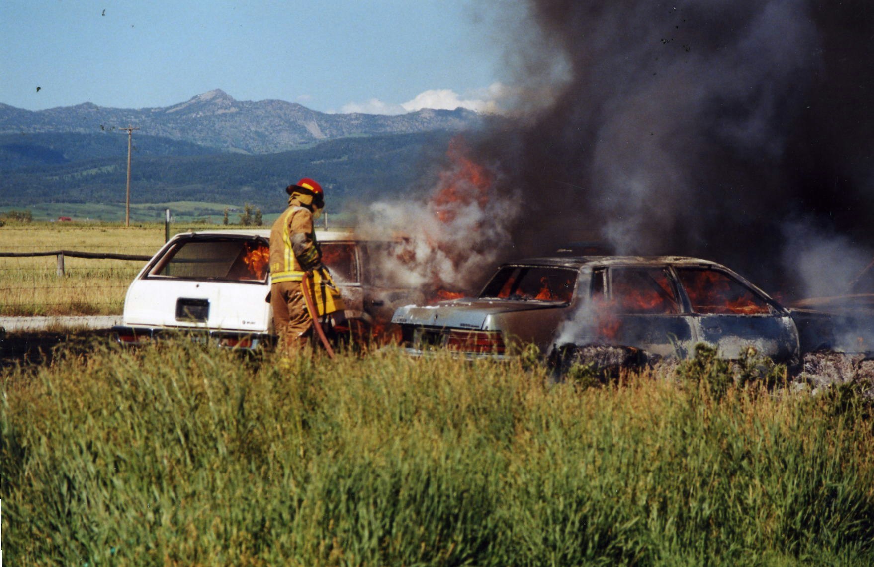 A firefighter by burning cars, with mountains in the background.