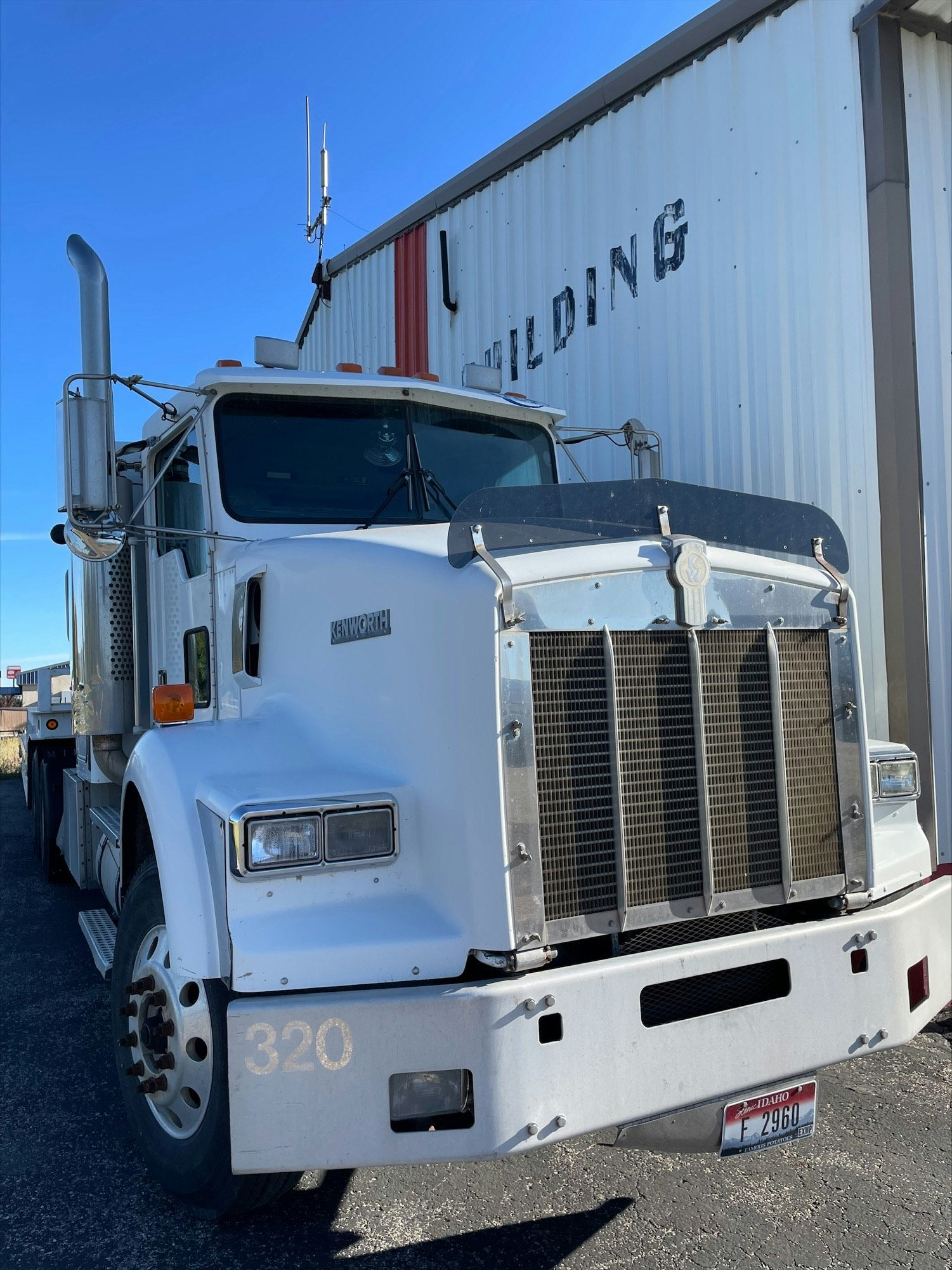 White semi-truck parked by a building with the word "BUILDING" on the siding.