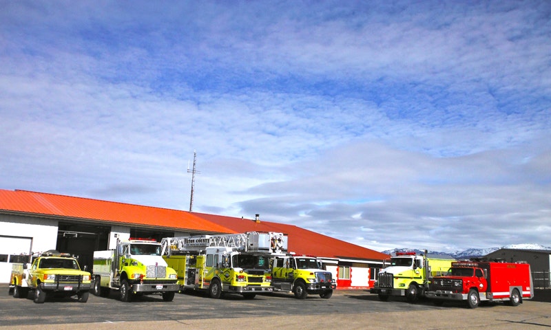 Fire trucks parked outside a fire station with a clear sky above.