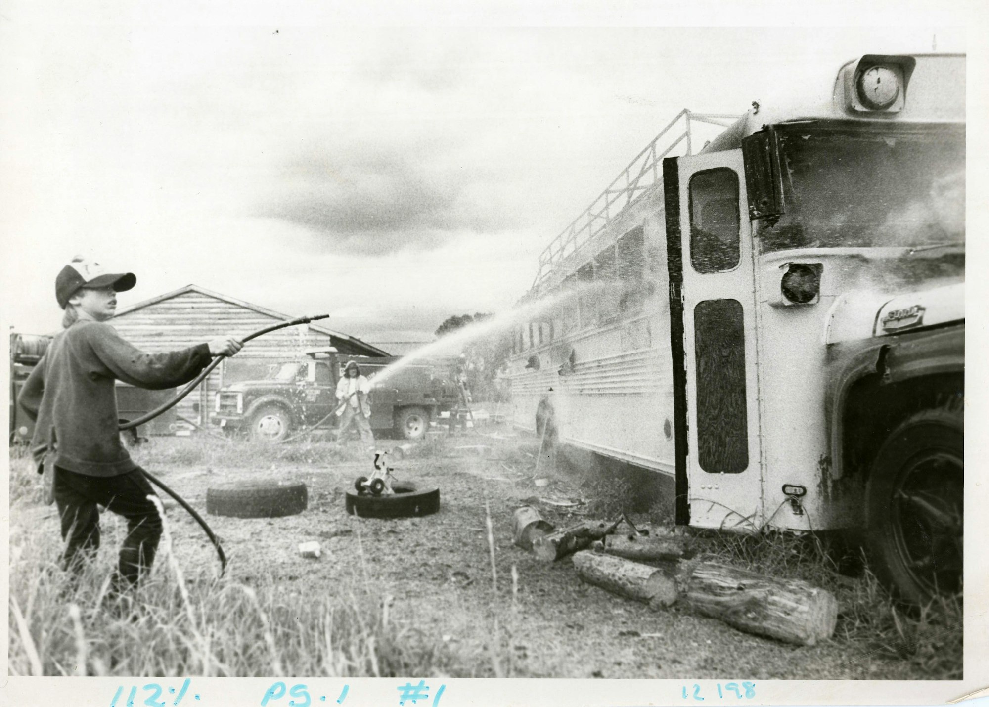 A child uses a hose near a bus and a fire truck, in a vintage photo.