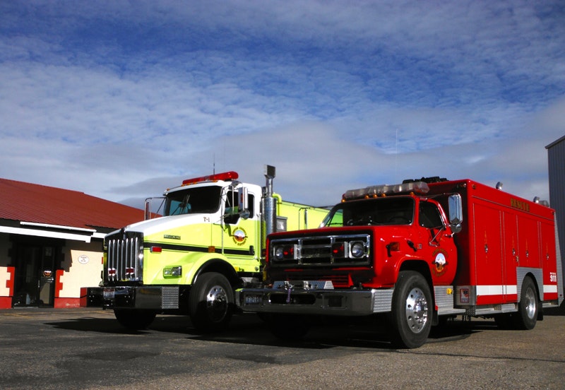 Two fire trucks parked outside a fire station under a clear sky.