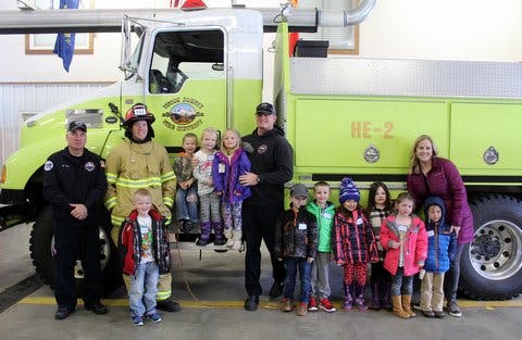 Group of people, including firefighters and children, in front of a fire truck.