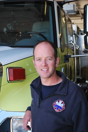 A person with an emergency services patch in front of a fire truck.