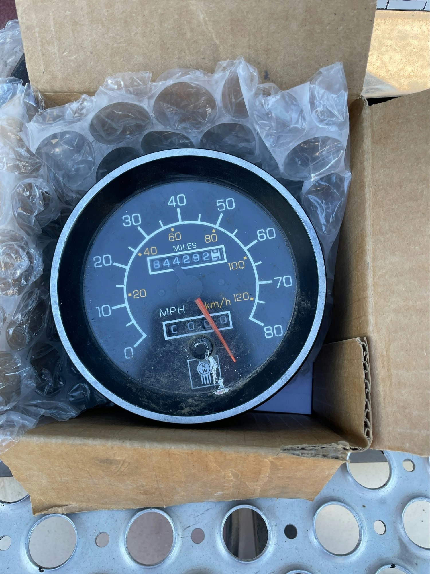 An old car speedometer and odometer, bubble wrap, cardboard box, part of an engine gasket.
