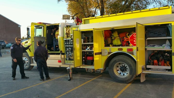 Firefighters beside a fire engine with equipment compartments open.