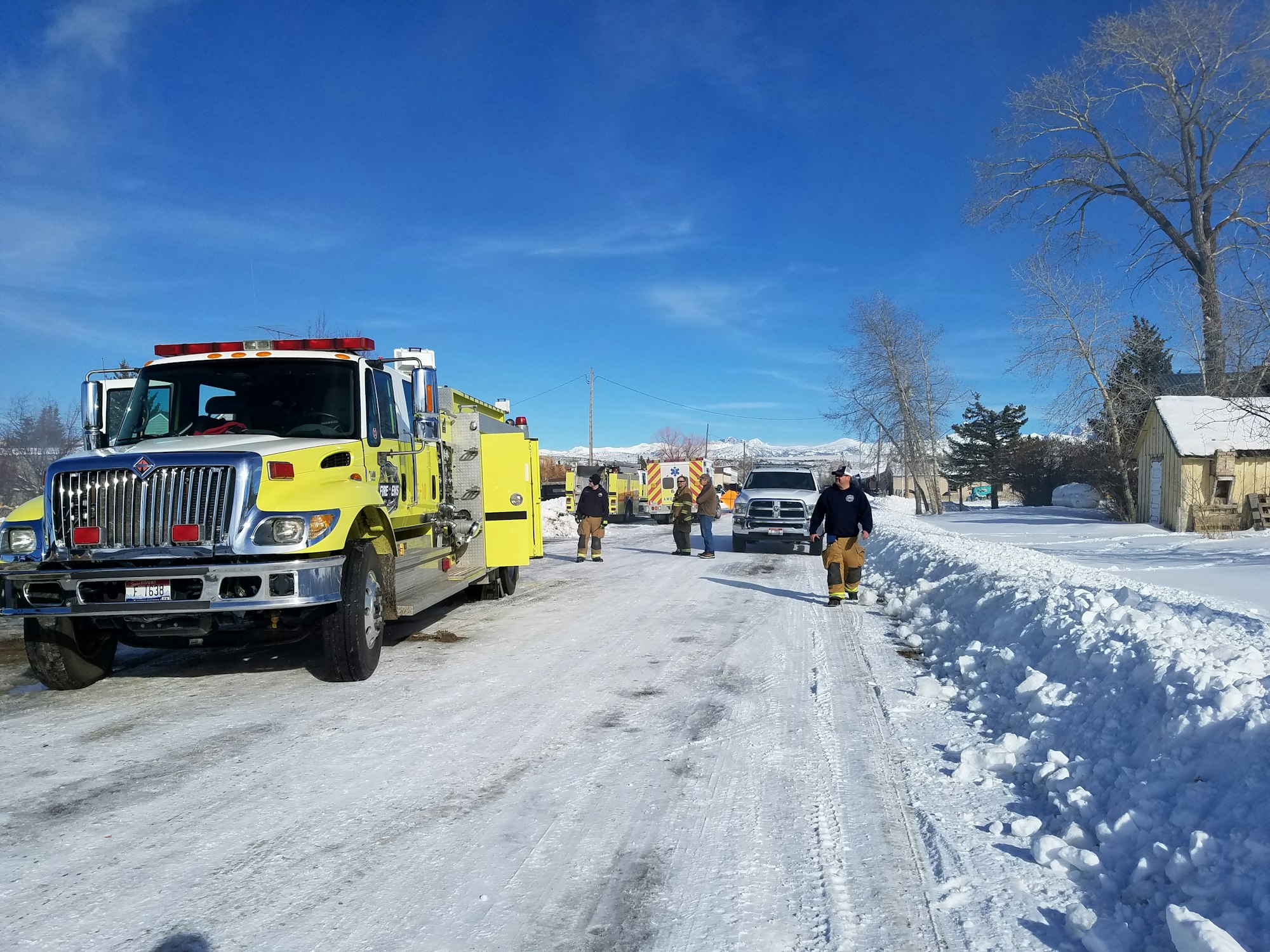 A fire truck on a snowy street with emergency personnel and clear blue skies.