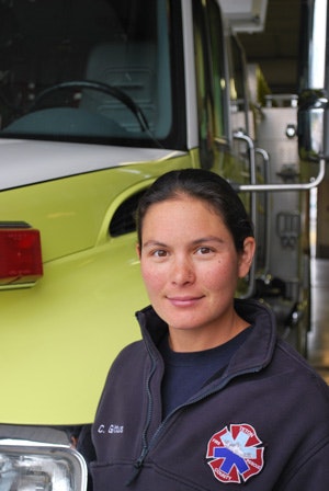 A person in a uniform with an EMS badge stands in front of an ambulance.