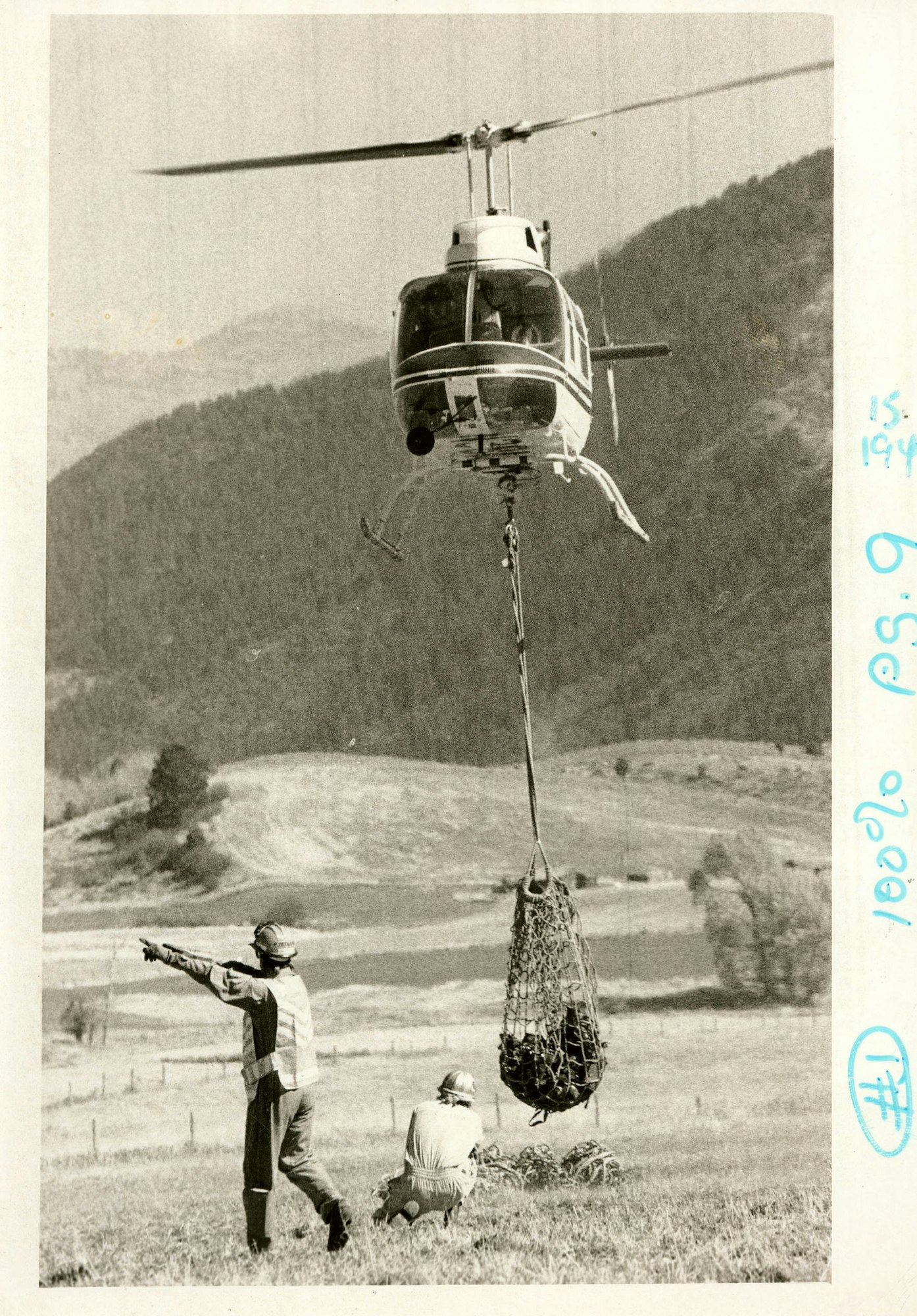 A helicopter lifting a net, with people guiding it on the ground.