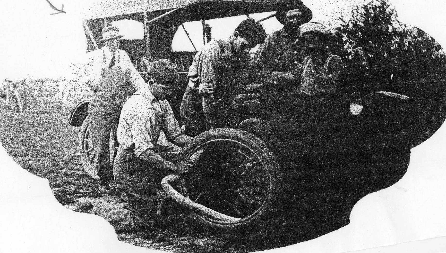 Vintage photo of people fixing a car tire, with onlookers.