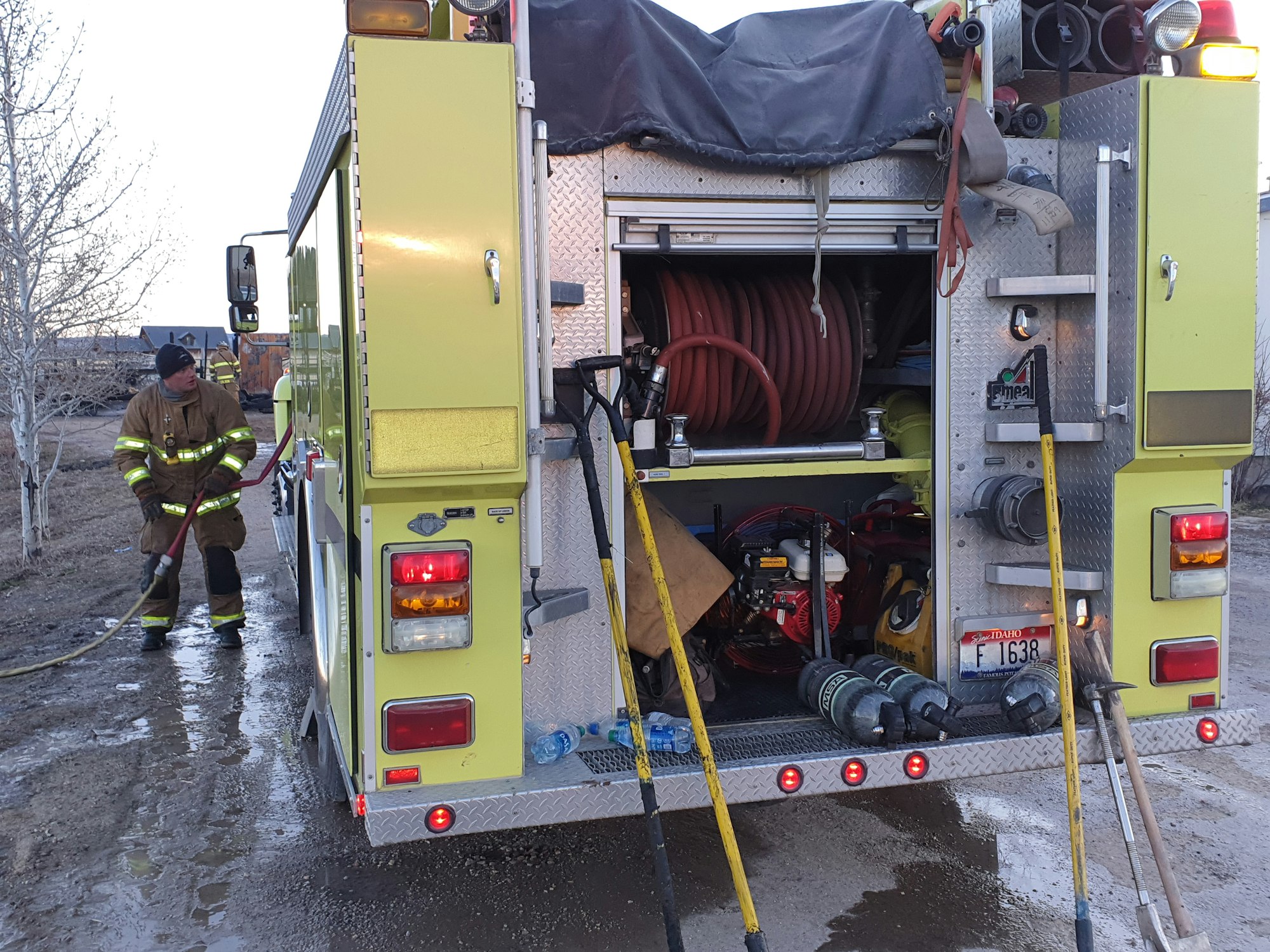 A firefighter handling a hose near a fire truck equipped with emergency gear.